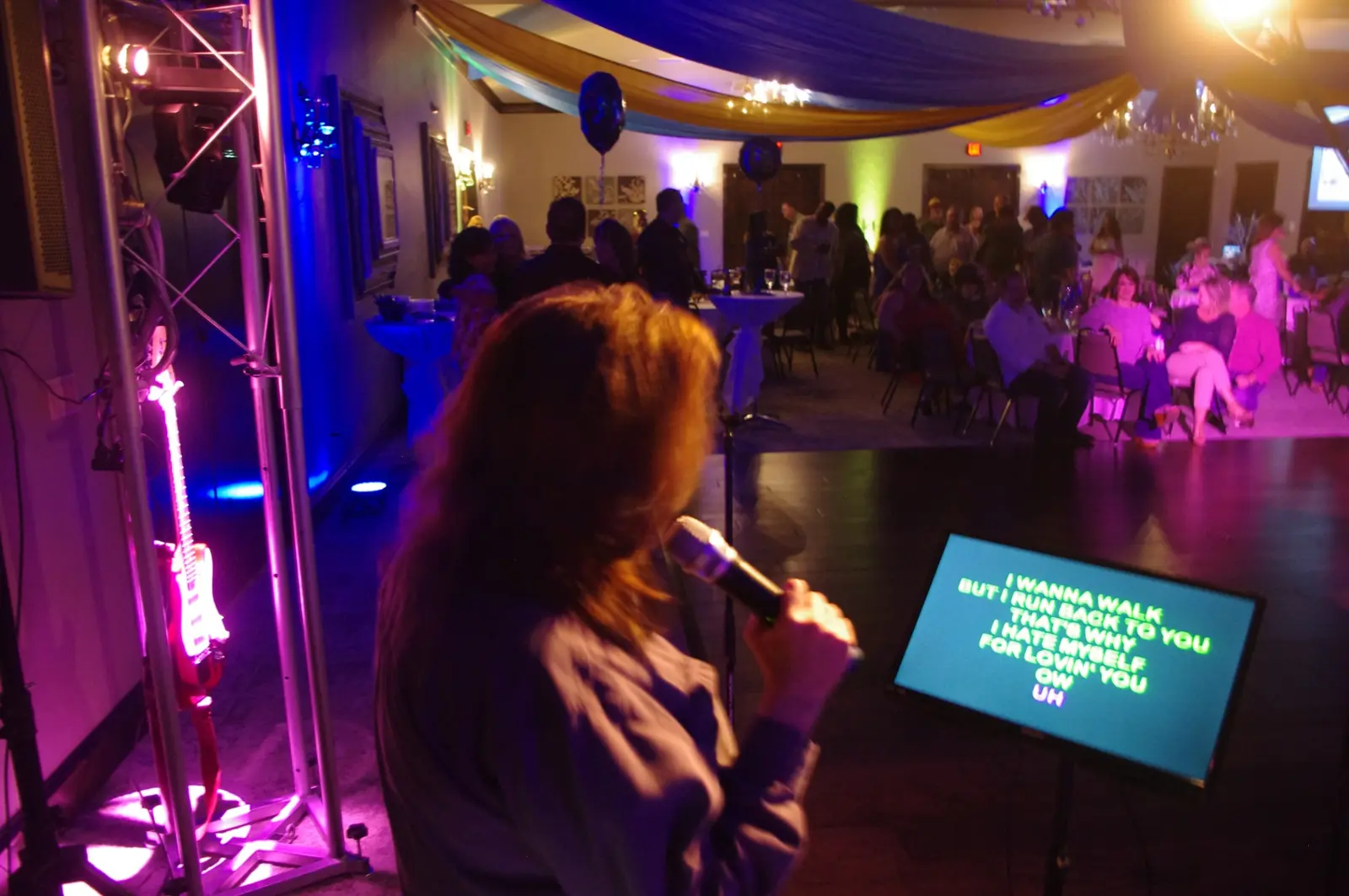A karaoke singer performing with the lyrics screen and audience visible