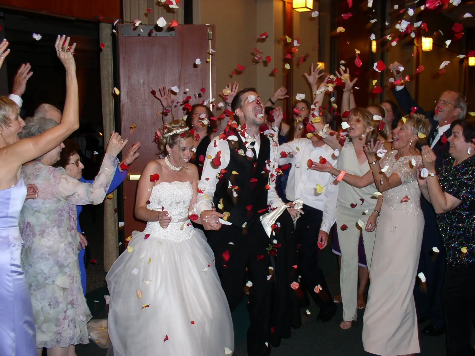 A newlywed couple laughing as their families shower them with rose petals